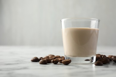 Photo of Coffee cream liqueur in glass and beans on white marble table, space for text