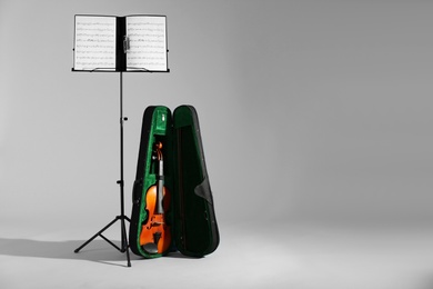 Violin in case and note stand with music sheets on grey background. Space for text