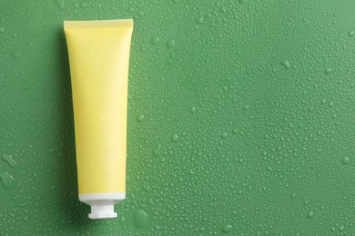 Moisturizing cream in tube on green background with water drops, top view. Space for text