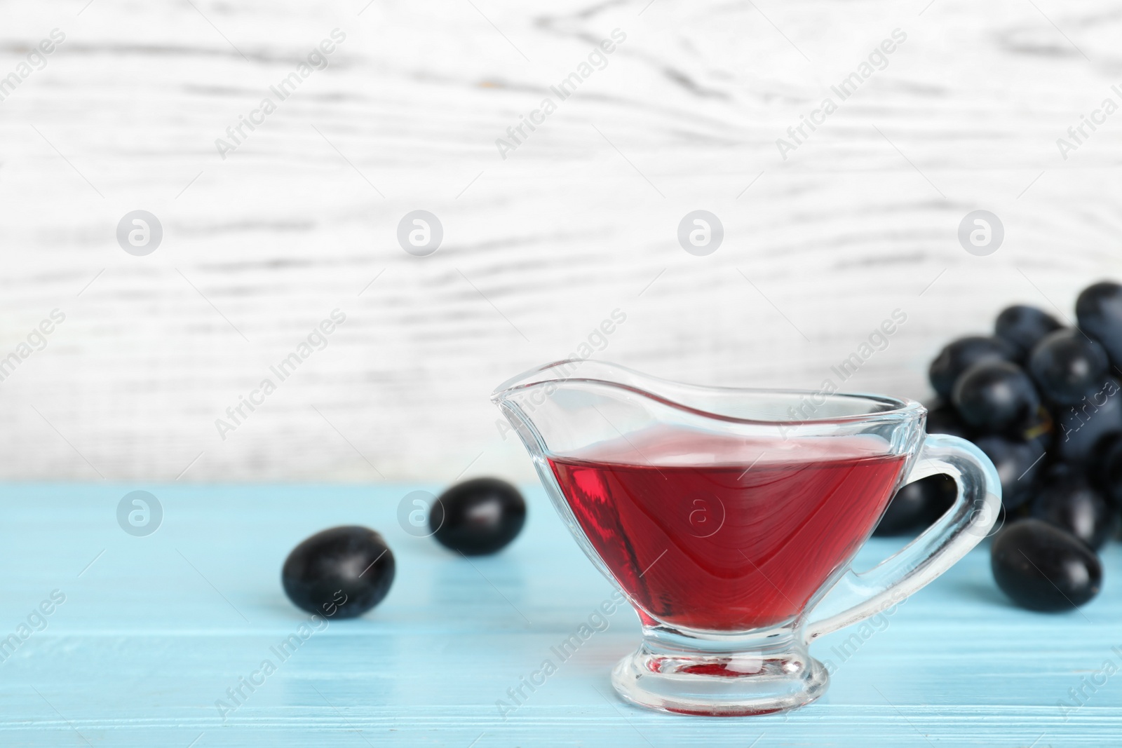 Photo of Glass gravy boat with wine vinegar and fresh grapes on wooden table. Space for text