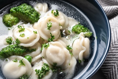 Bowl of tasty dumplings in broth on table, closeup