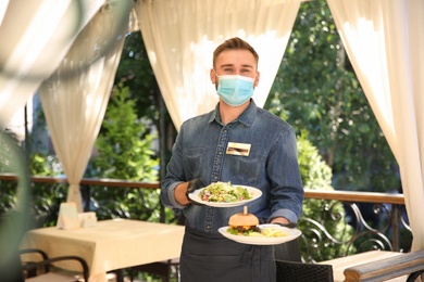 Photo of Waiter serving food in restaurant. Catering during coronavirus quarantine