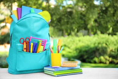 Bright backpack and school stationery on table outdoors, space for text