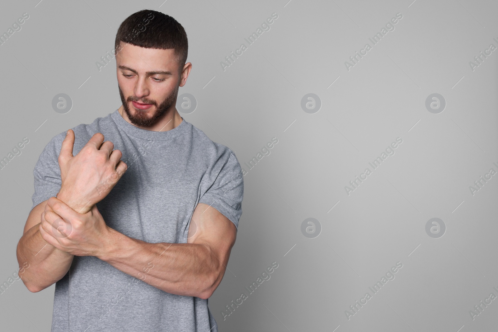 Photo of Man suffering from pain in his wrist on light grey background, space for text. Arthritis symptom