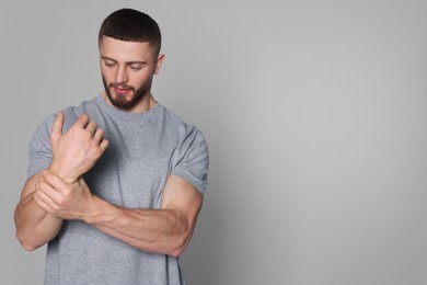 Photo of Man suffering from pain in his wrist on light grey background, space for text. Arthritis symptom