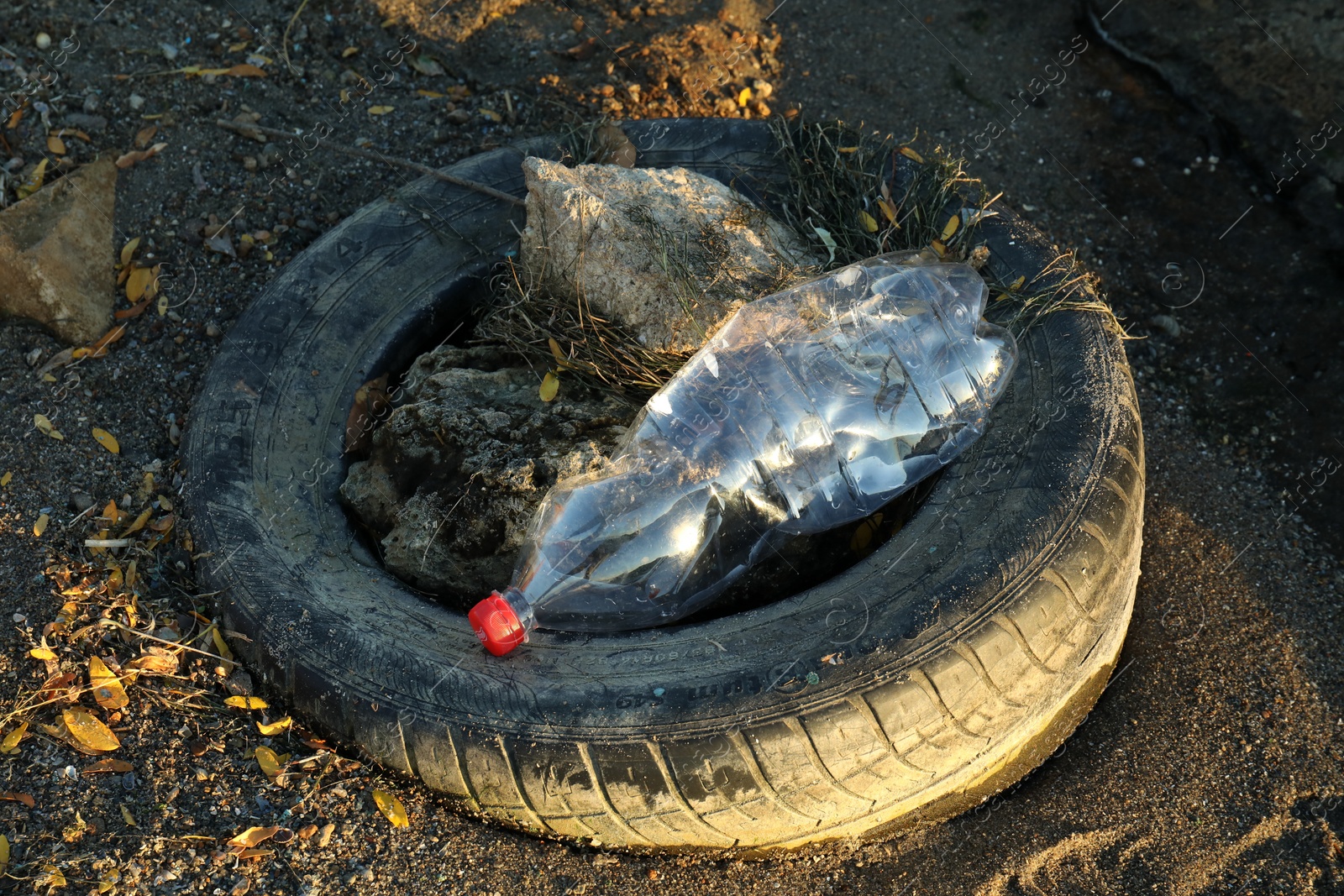 Photo of Used plastic bottle and tire on sand outdoors. Environment pollution