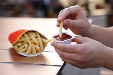 Photo of Lviv, Ukraine - September 26, 2023: Woman dipping McDonald's french fry into sauce at wooden table outdoors, closeup