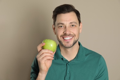 Smiling man with perfect teeth and green apple on color background