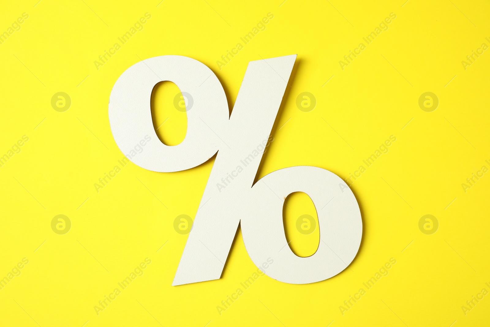 Photo of White percent sign on yellow background, top view