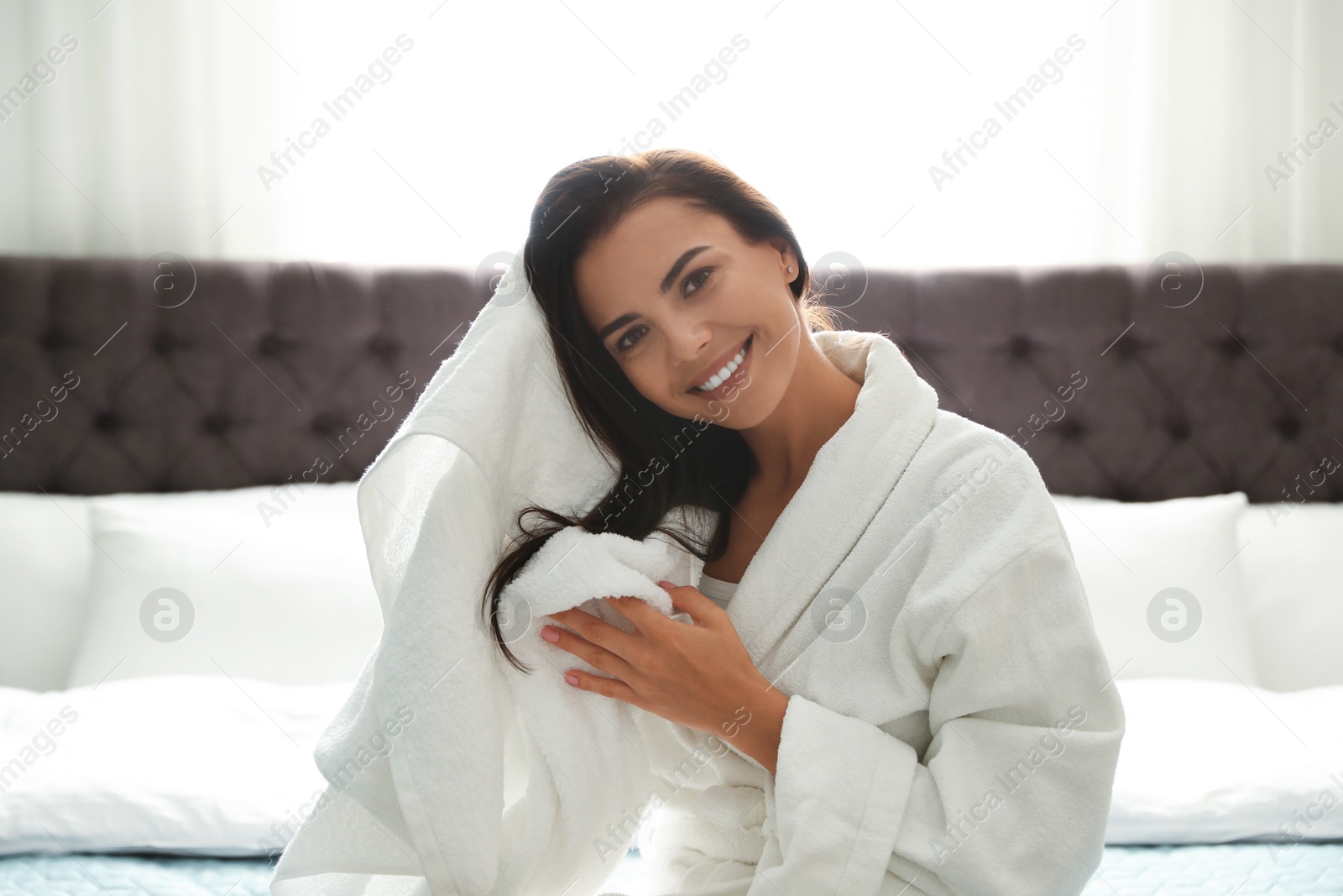 Photo of Pretty young woman drying hair with towel on bed in room