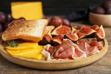 Photo of Delicious ripe figs, prosciutto and cheese served on wooden table, closeup