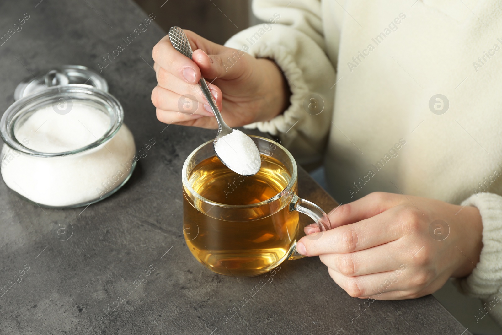 Photo of Woman adding sugar into aromatic tea at grey table, closeup