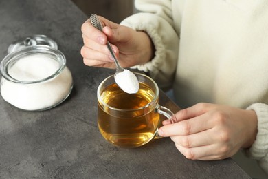 Woman adding sugar into aromatic tea at grey table, closeup