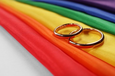 Photo of Rainbow LGBT flag and wedding rings on pink background, closeup