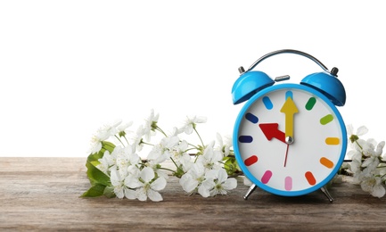 Photo of Alarm clock and branch with spring blossoms on wooden table against white background. Time change concept