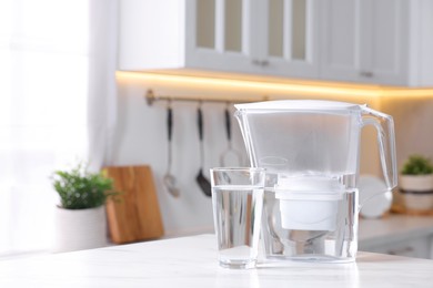 Photo of Water filter jug and glass on white marble table in kitchen, closeup. Space for text