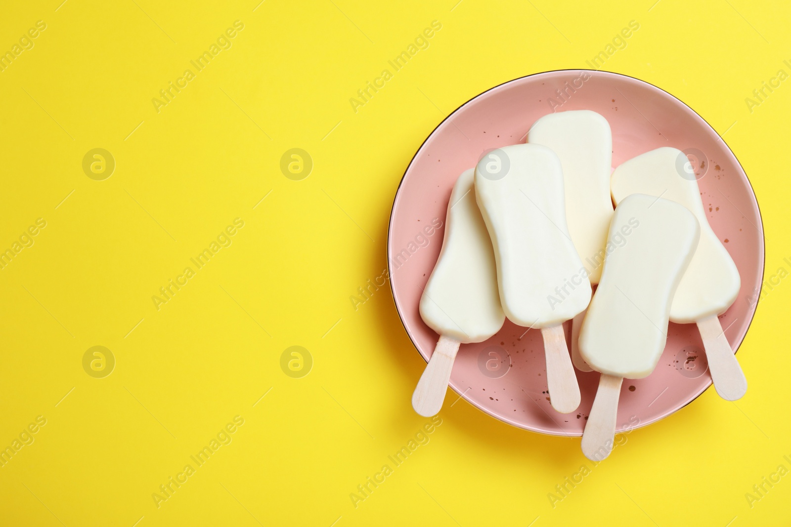 Photo of Plate with glazed ice cream bars on yellow background, top view. Space for text