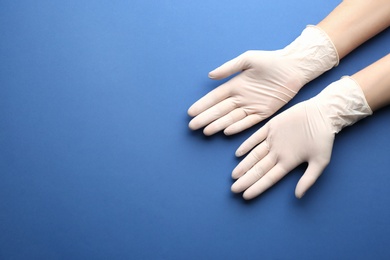 Person in medical gloves on blue background, top view. Space for text
