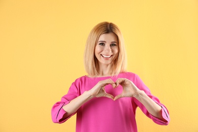 Portrait of woman making heart with her hands on color background. Space for text