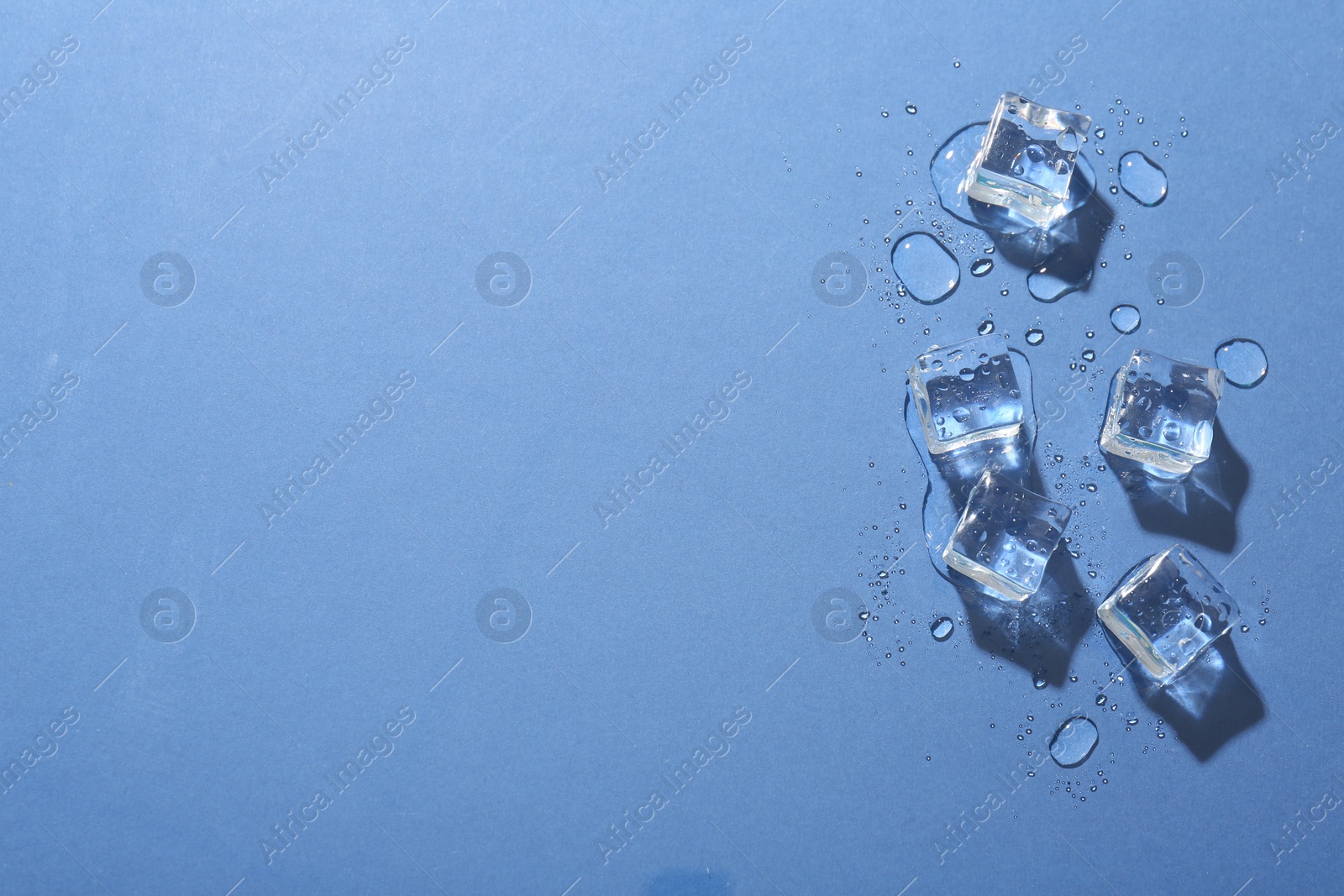 Photo of Melting ice cubes and water drops on blue background, flat lay. Space for text
