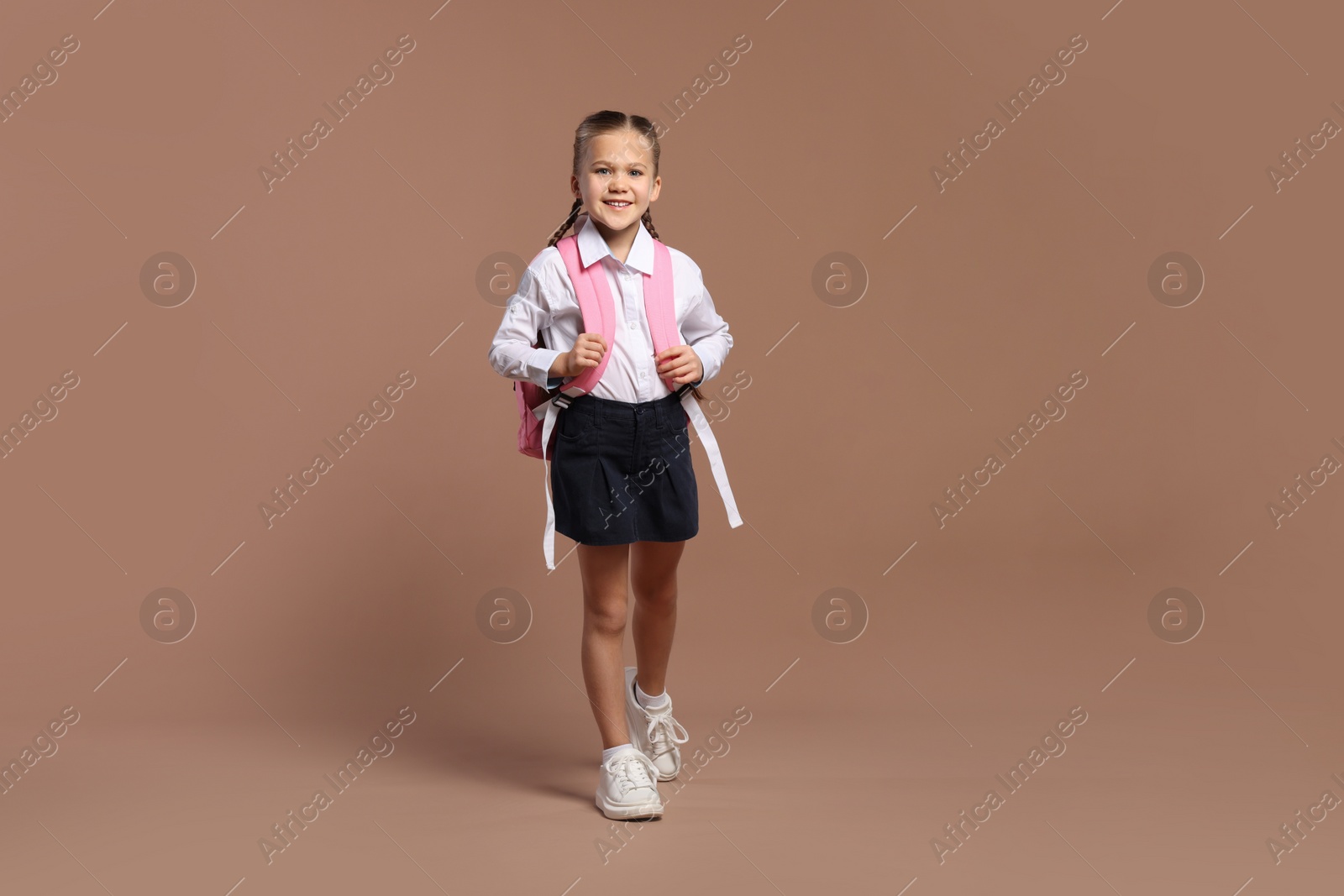 Photo of Happy schoolgirl with backpack on brown background