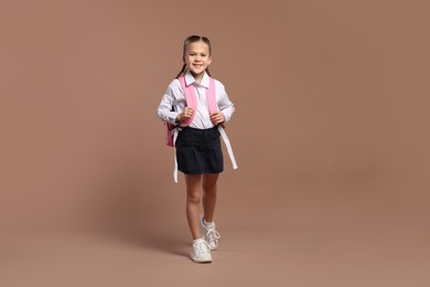 Photo of Happy schoolgirl with backpack on brown background