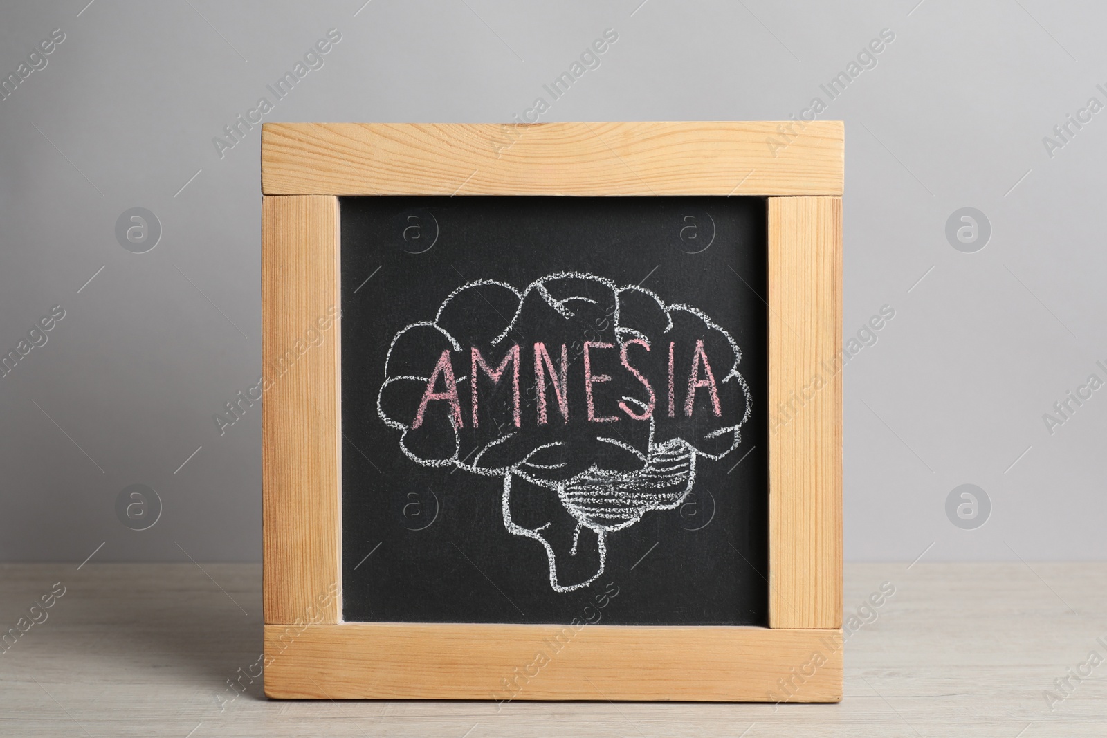 Photo of Small blackboard with drawn brain and word Amnesia on white wooden table