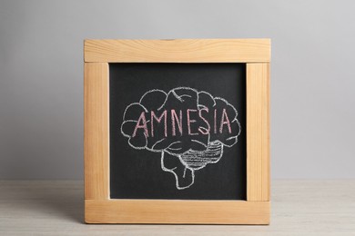 Small blackboard with drawn brain and word Amnesia on white wooden table