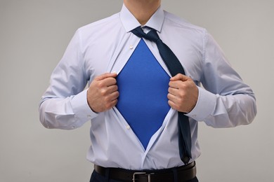 Photo of Businessman wearing superhero costume under suit on beige background, closeup