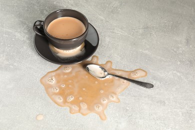 Photo of Cup, saucer and spoon near spilled coffee on grey table
