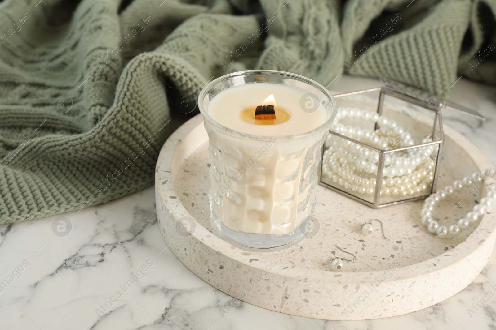 Photo of Tray with burning soy candle and beautiful bijouterie on white marble table