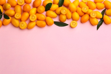 Fresh ripe kumquats with green leaves on pink background, flat lay. Space for text