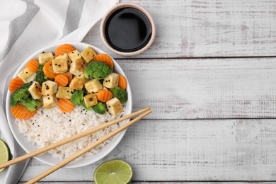 Photo of Delicious rice with fried tofu, broccoli and carrots served on white wooden table, flat lay. Space for text