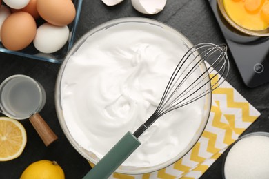 Photo of Bowl with whipped cream, whisk and ingredients on black table, flat lay