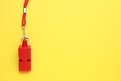 One red whistle with cord on yellow background, top view. Space for text