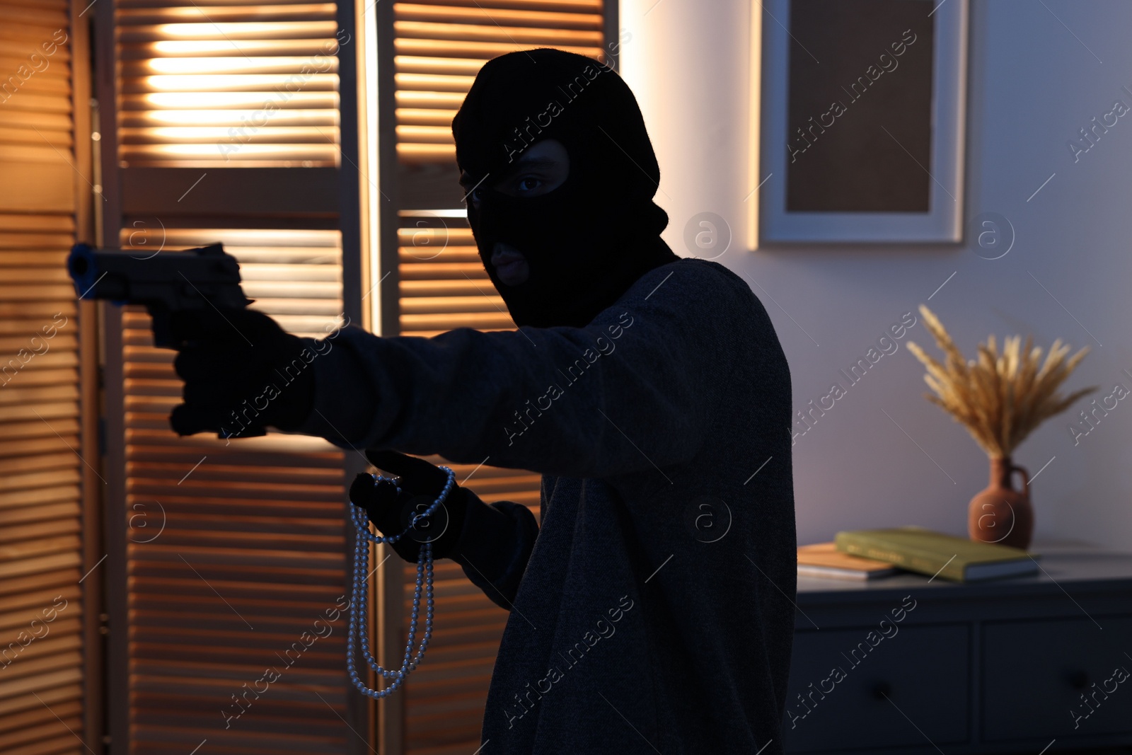 Photo of Thief with gun stealing jewels in foreign house. Burglary