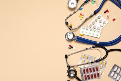 Photo of Stethoscopes and pills on beige background, flat lay. Space for text