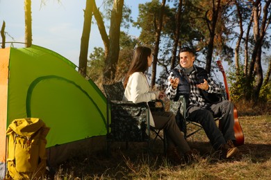 Couple resting in camping chairs near tent outdoors