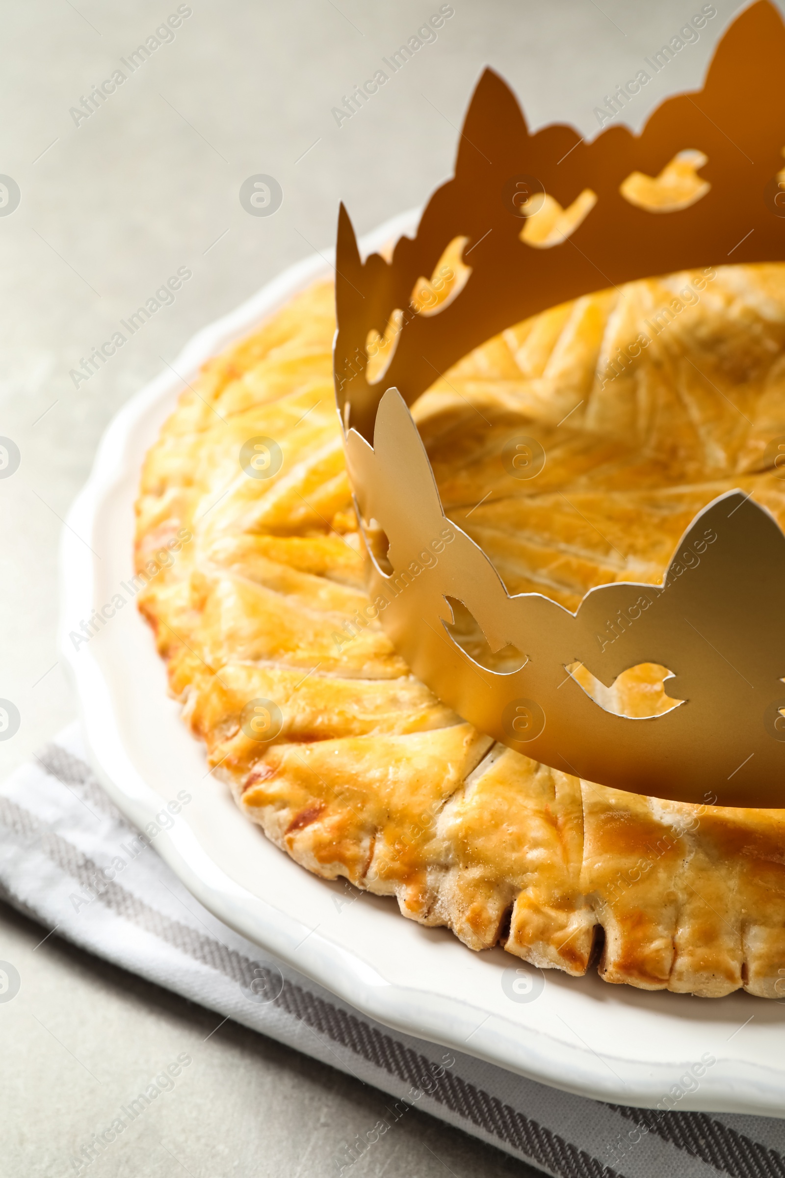 Photo of Traditional galette des Rois with paper crown on table, closeup