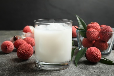 Photo of Glass with lychee juice and fresh fruits on grey table