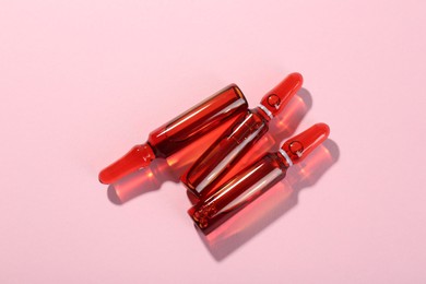 Glass ampoules with liquid on pink background, top view