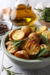 Photo of Bowl with tasty baked potato and aromatic rosemary on white tiled table, closeup