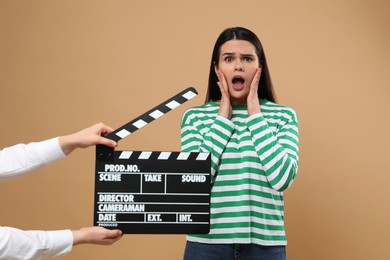 Photo of Emotional actress performing while second assistant camera holding clapperboard on beige background. Film industry