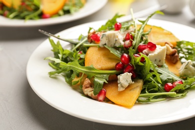 Photo of Delicious persimmon salad with pomegranate and arugula served on light grey table, closeup