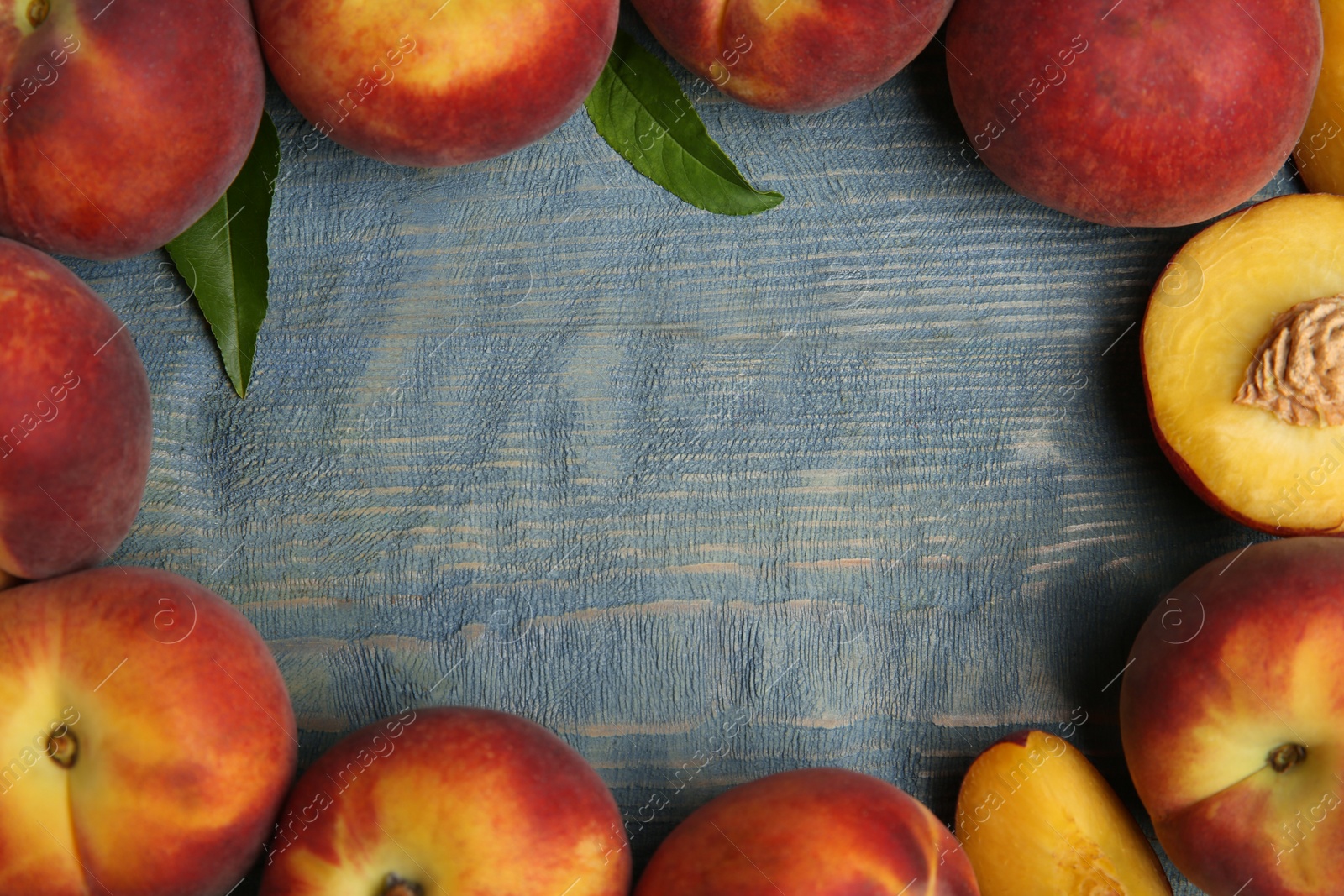 Photo of Frame made of fresh peaches on blue wooden table, top view with space for text