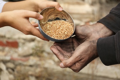 Photo of Woman giving poor homeless man bowl of wheat outdoors, closeup