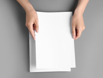 Photo of Woman holding blank paper sheets for brochure at grey table, top view. Mock up