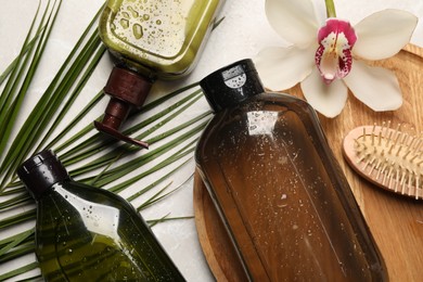 Photo of Wet shampoo bottles, hair brush, palm leaf and orchid flower on grey table, flat lay