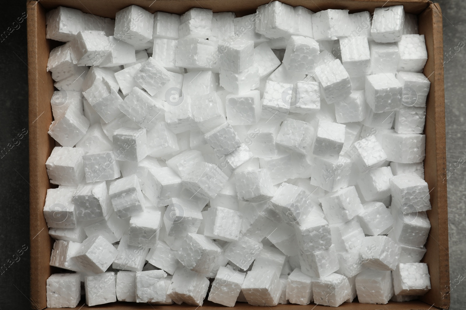 Photo of Cardboard box filled with polystyrene styrofoam pieces on grey background, top view