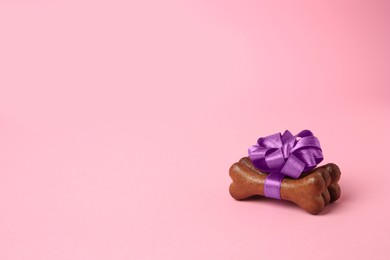 Photo of Bone shaped dog cookies with purple bow on pink background, space for text